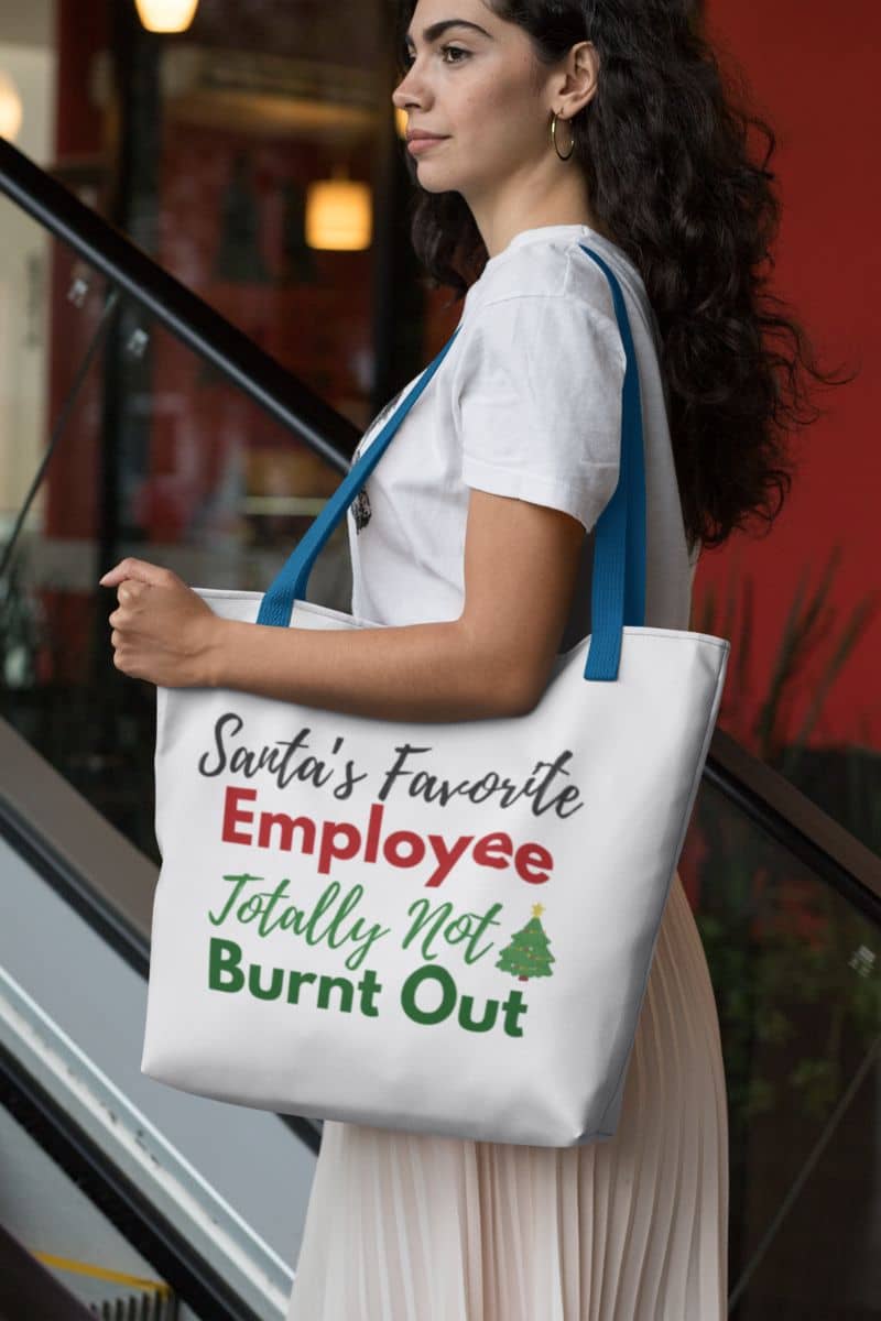 Reusable shopping tote with a woman holding a tote bag with humorous text 'Santa’s Favorite Employee Totally Not Burnt Out'