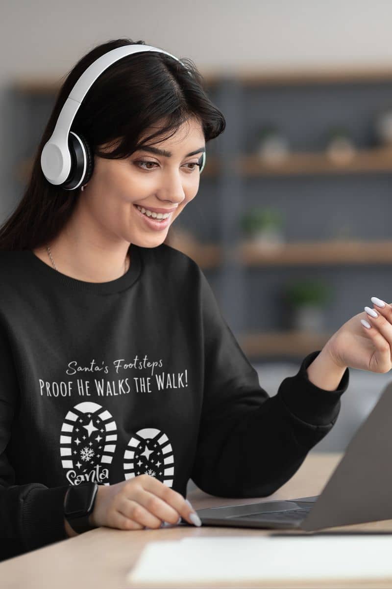Santa's Footsteps Sweatshirt with the girl wearing headphones and looking at the laptop with a bright smile