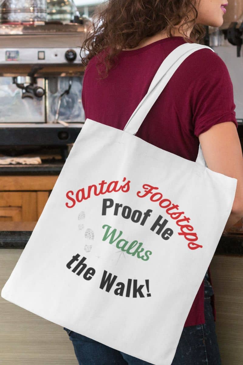 Santa's footsteps tote bag with a person holding a tote bag with text 'Santa's Footsteps - Proof He Walks The Walk!' in a casual setting
