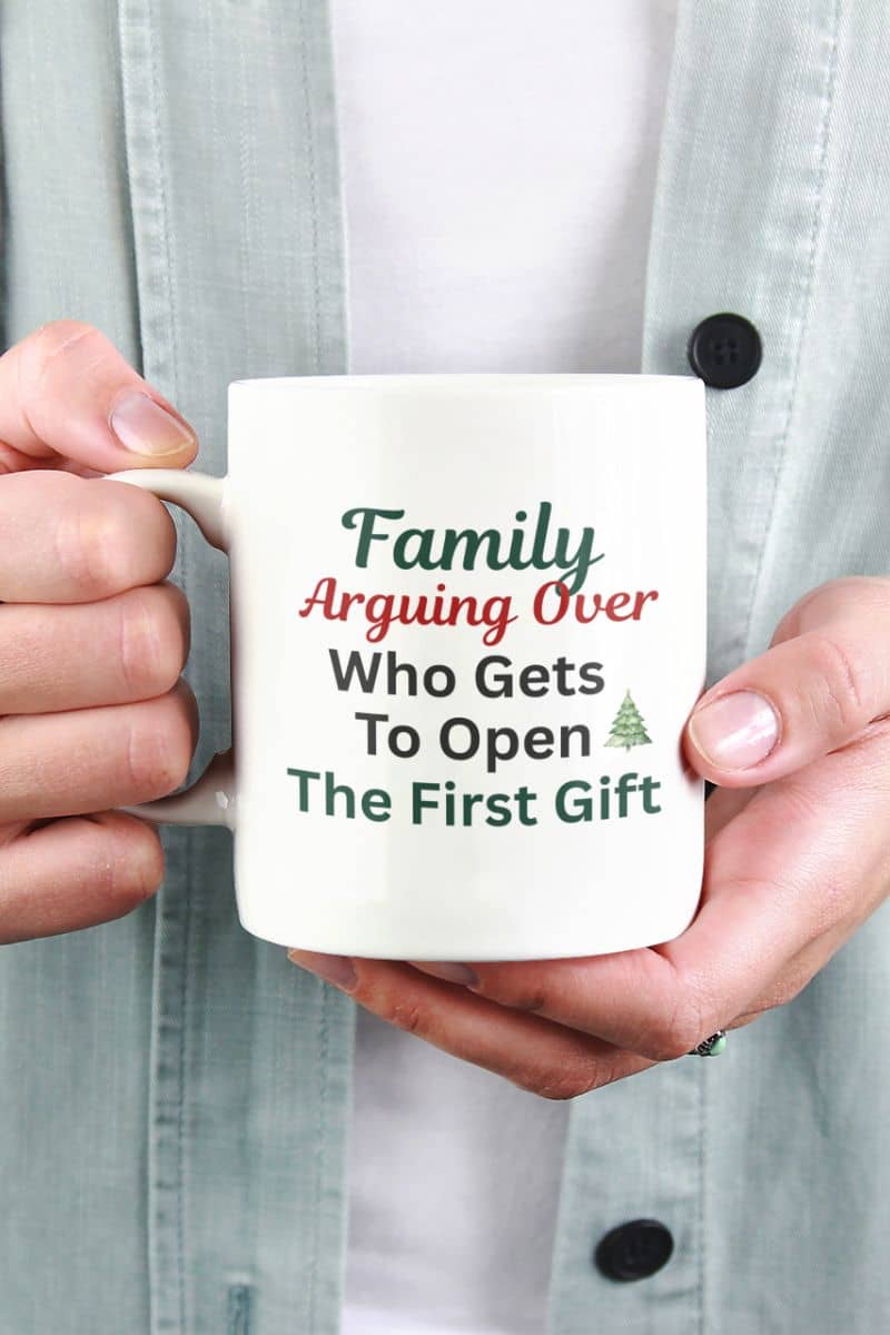 Sarcastic christmas gift mug with a person holding a mug with humorous text 'Family: Arguing Over Who Gets To Open The First Gift'