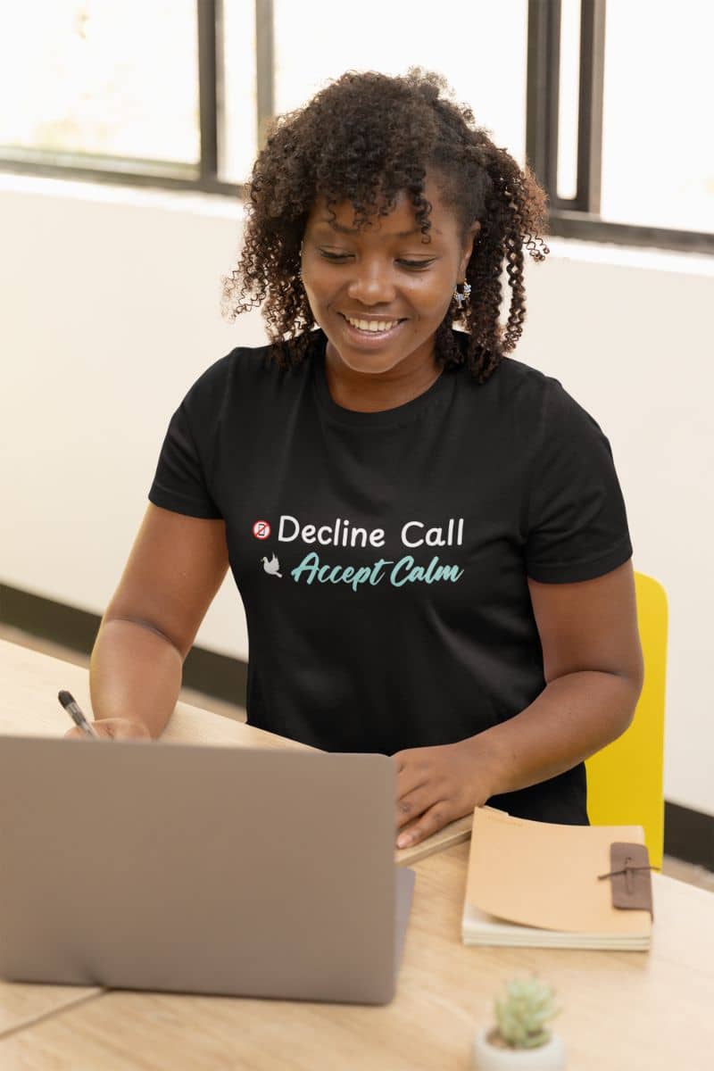 Slow living graphic tee with a person wearing a black t-shirt with text 'Decline Call Accept Calm', sitting at a desk with a laptop.