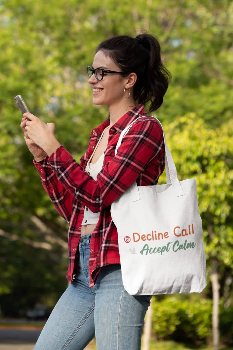 Spiritual lifestyle bag with a woman holding a phone and a tote bag with text  'Decline Call, Accept Calm' outdoors