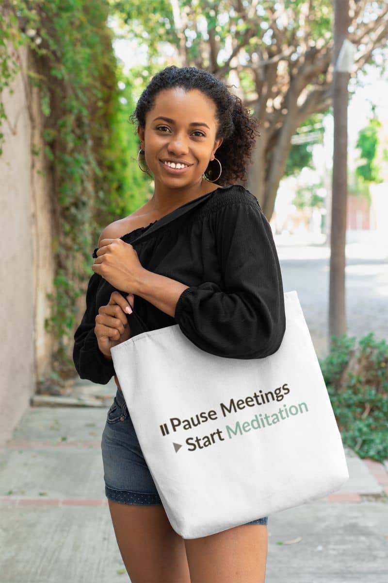 Spiritual sass tote bag with a woman holding a tote bag with text 'Pause Meetings Start Meditation' outdoors.