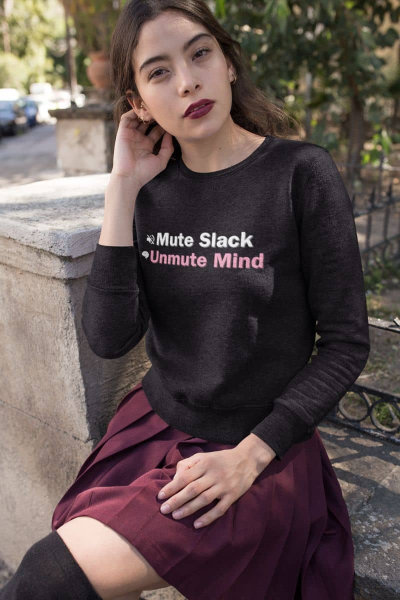 Tech-free lifestyle sweater with a woman wearing a black sweater with text 'Mute Slack, Unmute Mind', sitting outdoors.