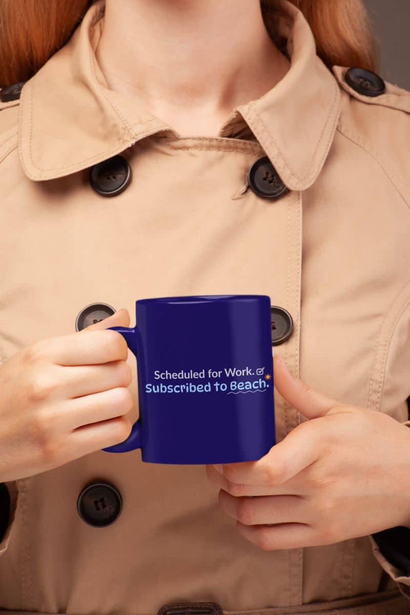 Travel mug with a person holding a blue mug, featuring the text 'Scheduled for Work. Subscribed to Beach', wearing a beige coat.