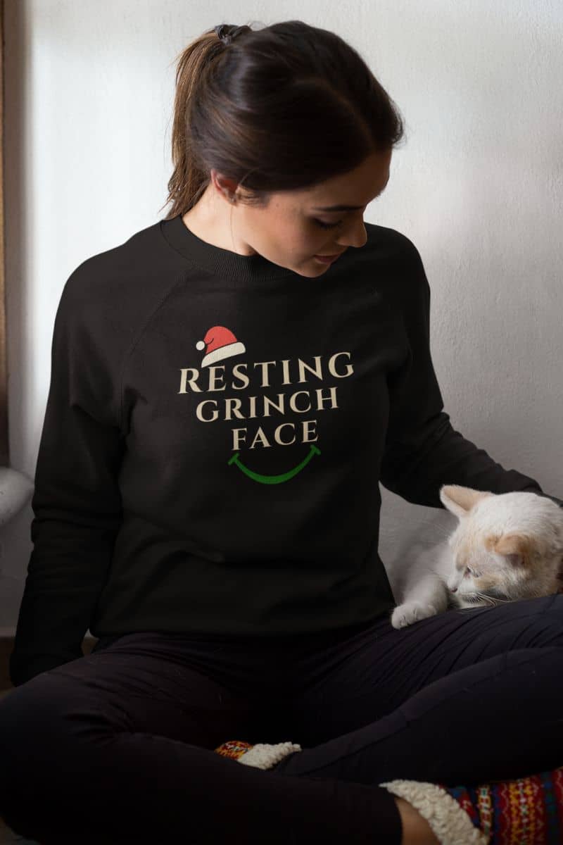 Warm Holiday pullover with a person wearing a black sweatshirt with 'Resting Grinch Face' text, sitting with a cat.