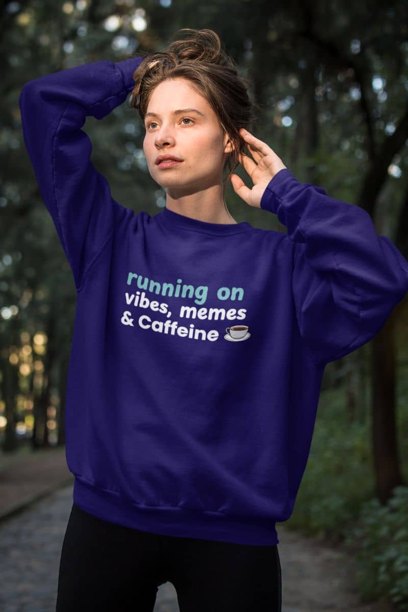 Warm and soft fleece sweatshirt with a person wearing a blue sweatshirt with text 'Running on Vibes, Memes & Caffeine' in a forest setting