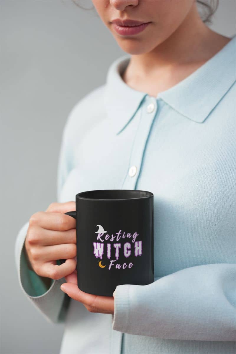 Witch humor tea cup with a person holding a black mug with 'Resting Witch Face' text, wearing a light blue shirt.