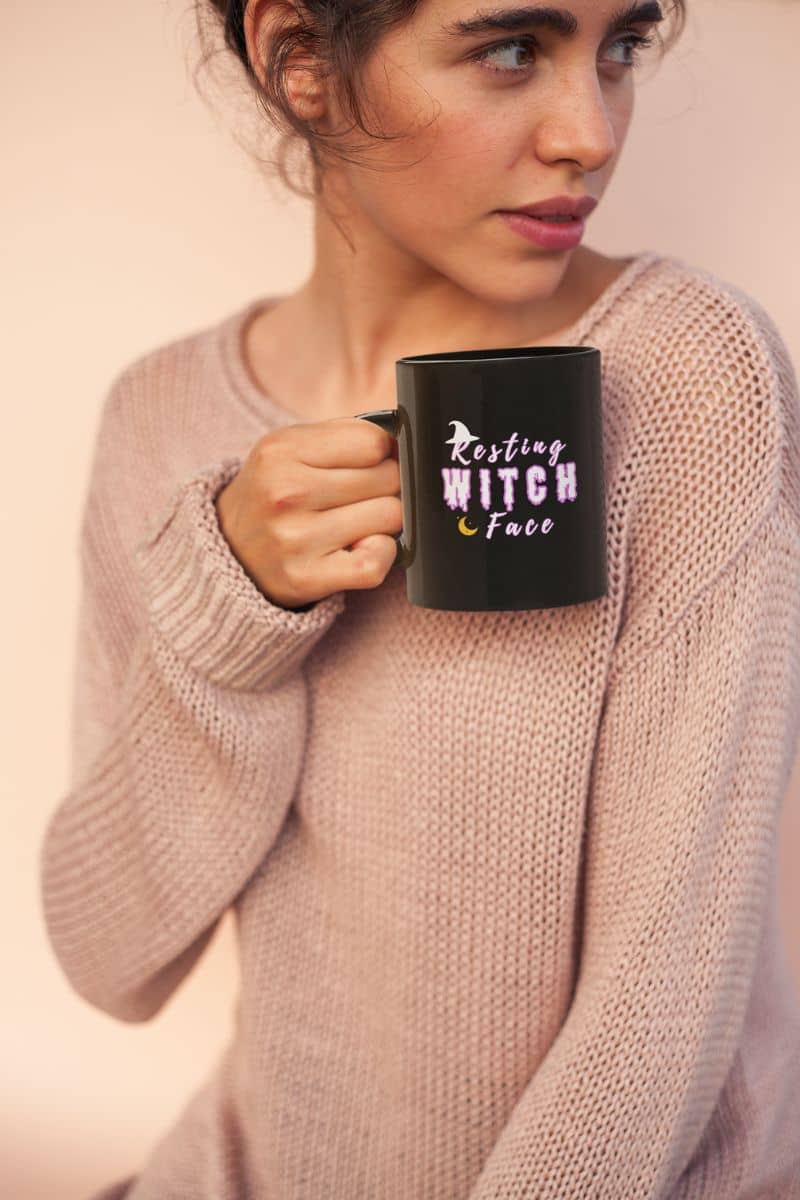 Witch life coffee mug with a woman holding a black mug with 'Resting Witch Face' text against a plain background
