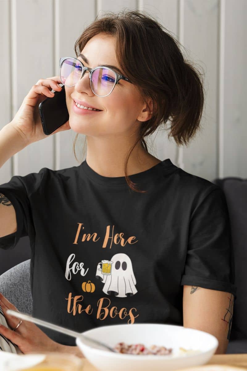 Witchy funny T-shirt with a girl wearing a shirt that reads “I’m Here for the Boos” while talking on the phone.