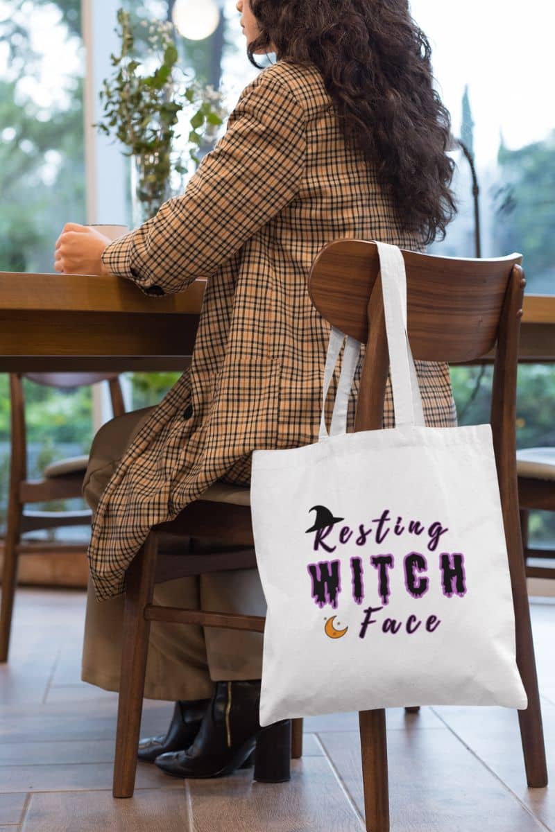 Witchy reusable bag with a person sitting at a table with a tote bag featuring 'Resting Witch Face' text.