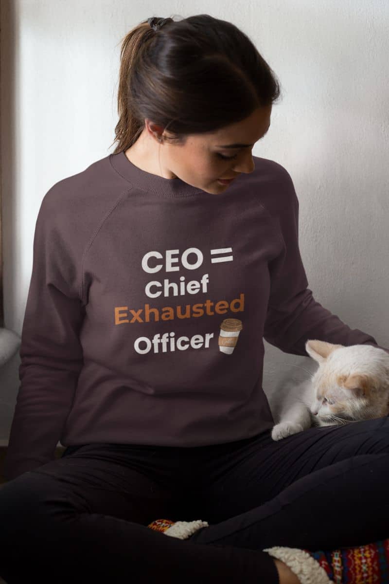 Work burnout sweater with a person wearing a sweatshirt with 'CEO = Chief Exhausted Officer' text sitting with a cat.