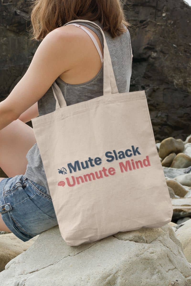 Work-from-home tote bag with a person holding a tote bag with text 'Mute Slack Unmute Mind' on a rocky surface