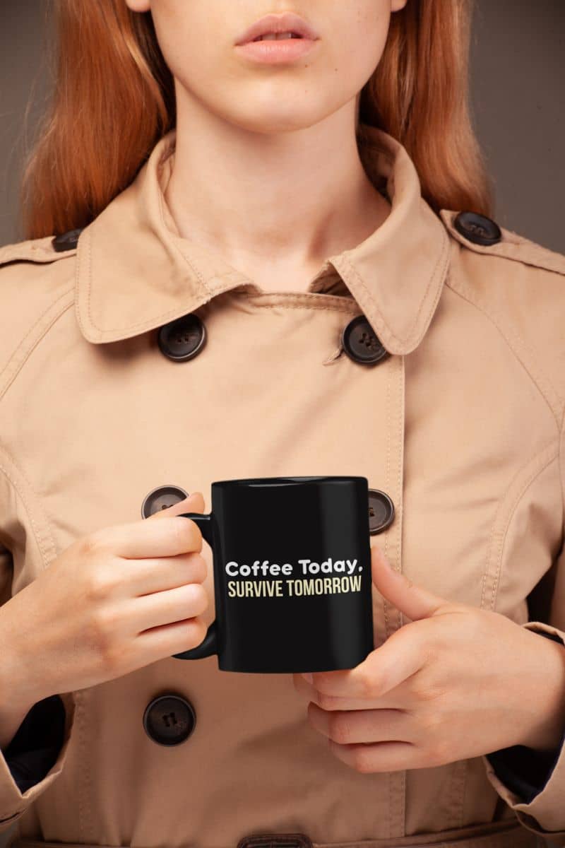 Workday motivation coffee mug with a person holding a black mug with text, wearing a beige trench coat.