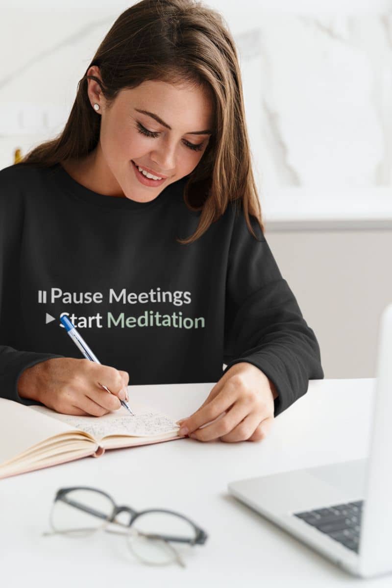 Yoga and wellness sweatshirt with a woman wearing a black sweatshirt with text, sitting at a table with a notebook and pen.