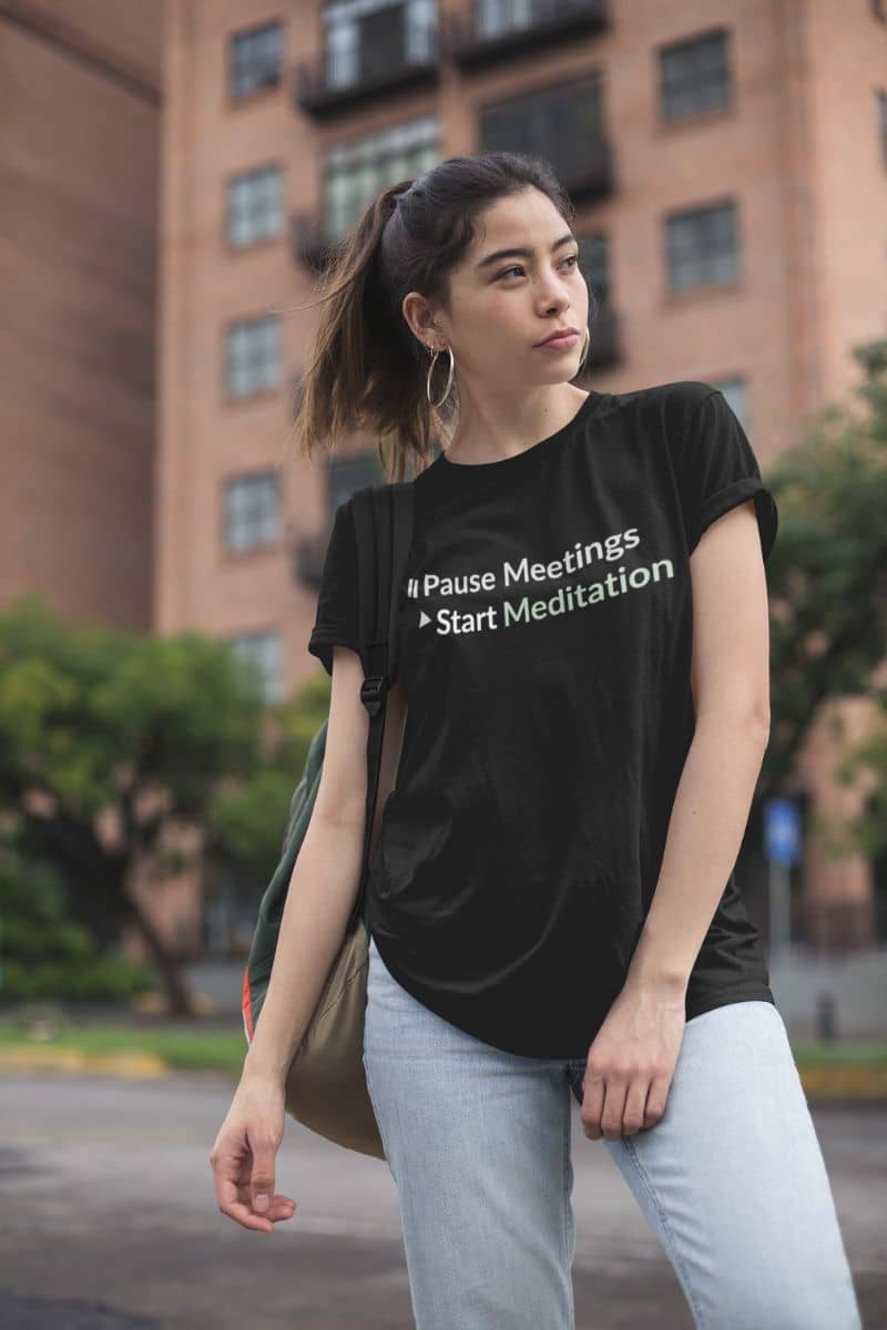 Yoga humor t-shirt with a woman wearing a black t-shirt with text, standing outdoors with a building in the background