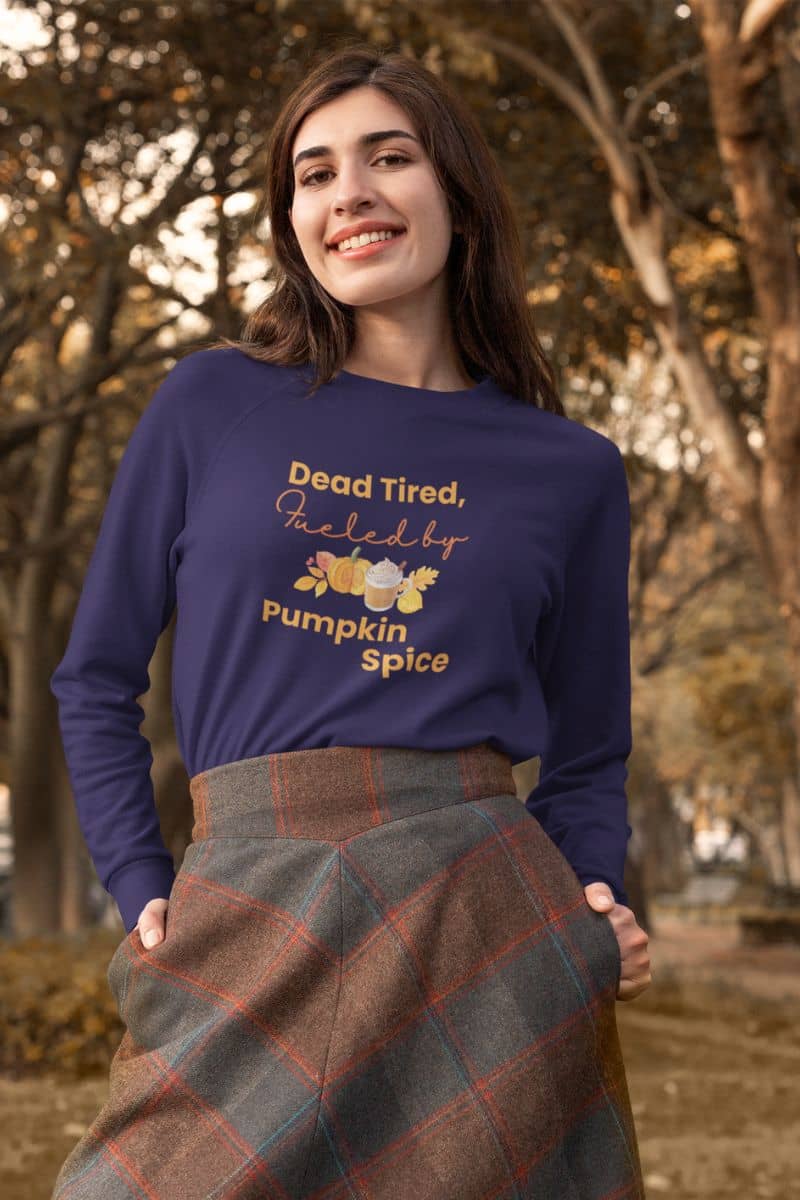 autumn coffee lover sweater with a woman wearing a blue sweater with 'Dead Tired, Fueled by Pumpkin Spice' text in an outdoor setting