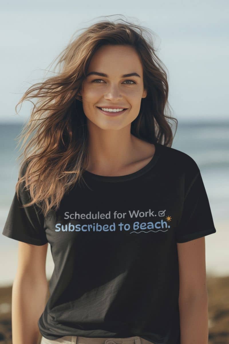 Beach themed tee shirts featuring a woman by the ocean wearing a black T-shirt with the phrase “Scheduled for Work. Subscribed to Beach.”
