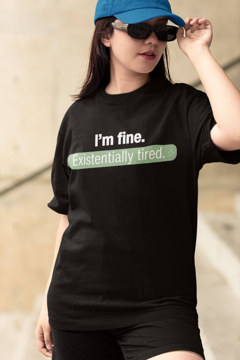 burnout humor t-shirt with a person wearing a black t-shirt with humorous text 'I’m fine. Just existentially tired'.
