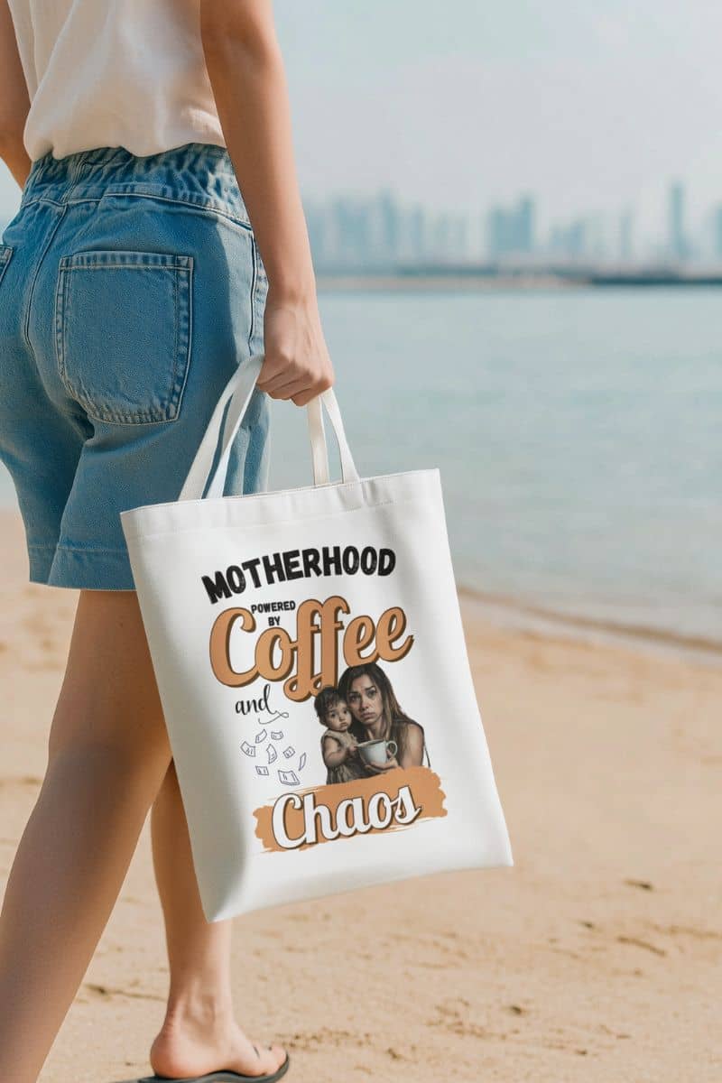 coffee and chaos tote with a person holding a tote bag with a humorous quote about motherhood on a beach.