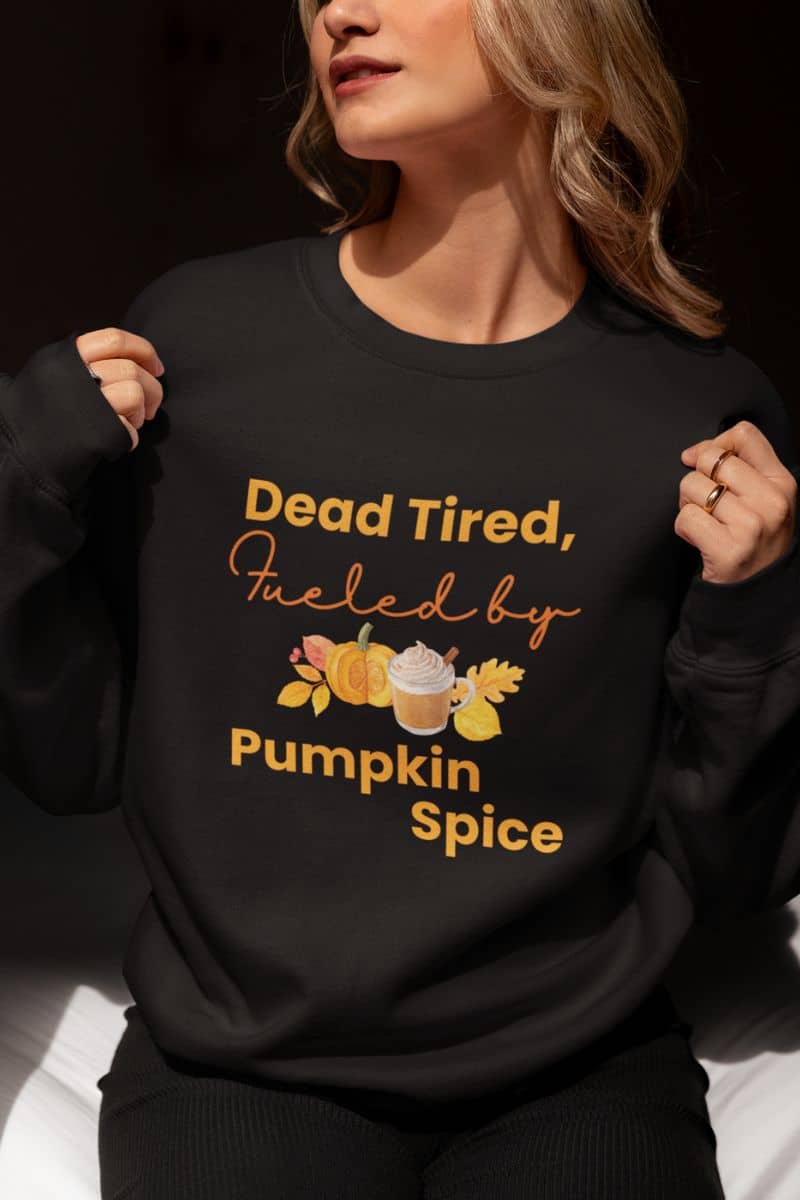cozy fall pullover with a person wearing a black sweatshirt with yellow text 'Dead Tired, Fueled by Pumpkin Spice' on a dark background