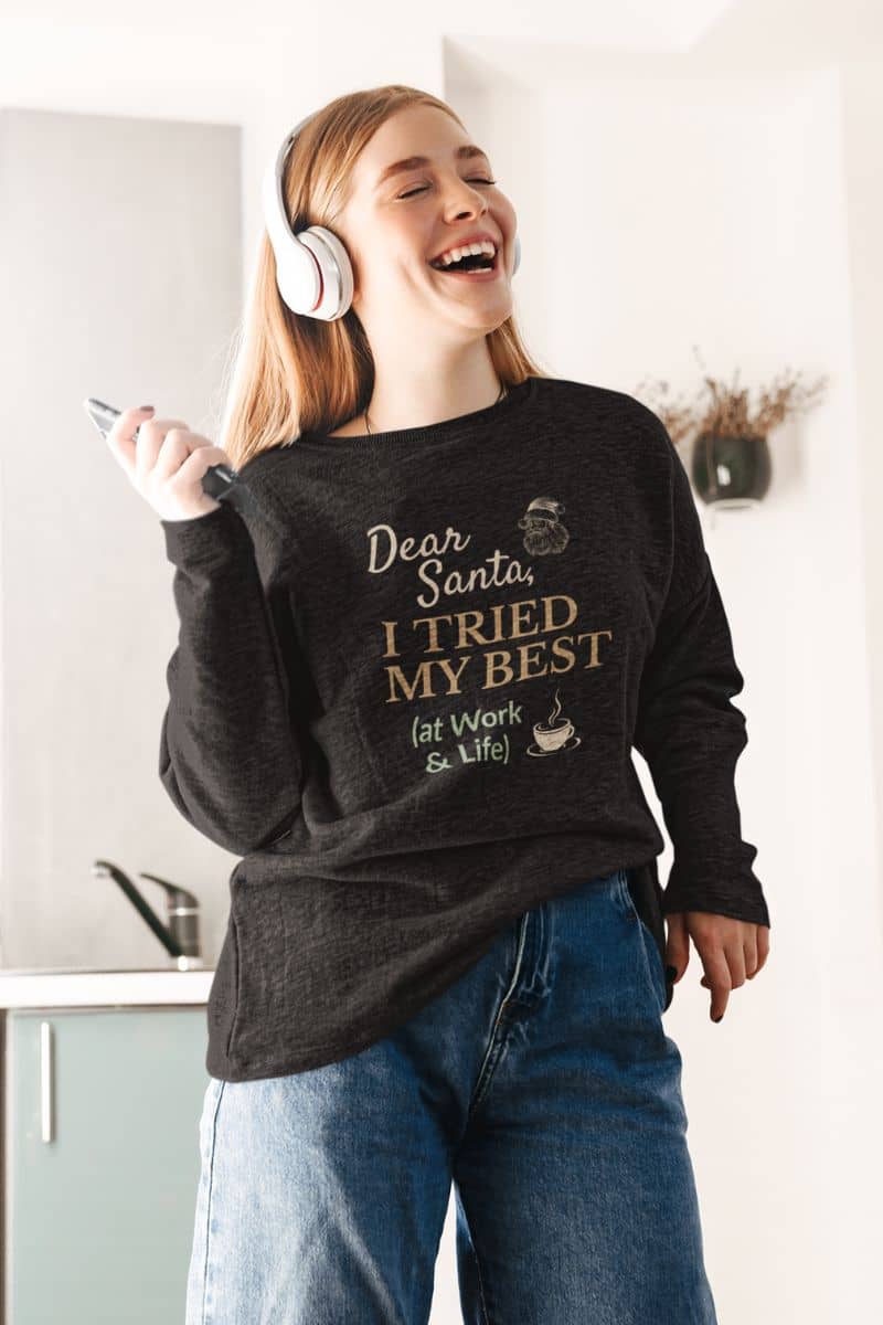 cozy holiday pullover with a person wearing a sweatshirt with text 'Dear Santa, I tried my best (at work & life)', laughing in a kitchen.