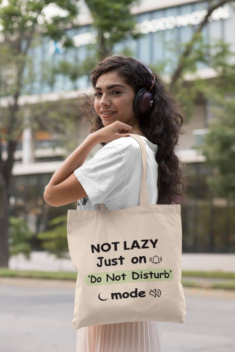 do not disturb tote bag with a woman wearing headphones and holding a tote bag with text 'NOT LAZY, Just on 'Do Not Disturb' mode' in an urban setting