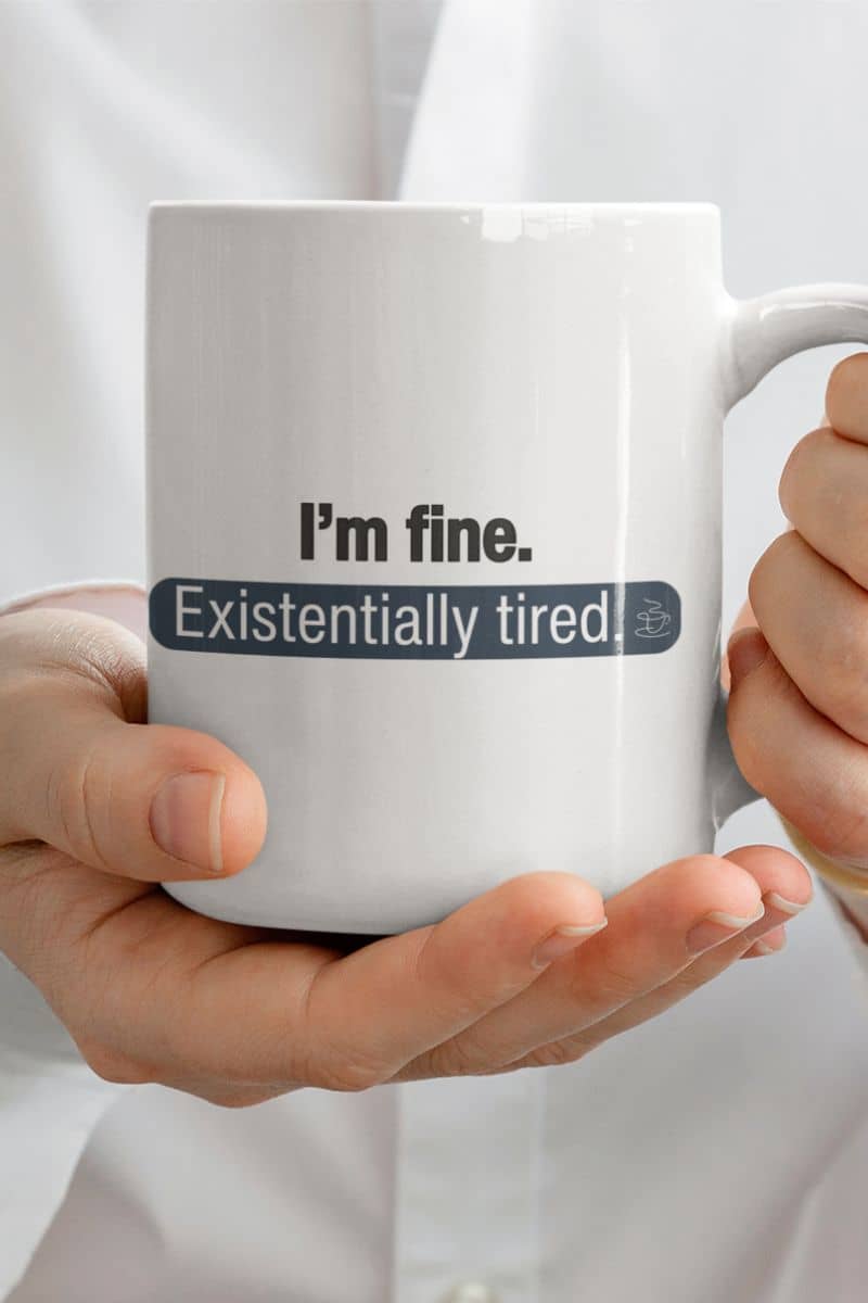 existential humor drinkware with a white mug held by hands with text 'I'm fine. Existentially tired' on a white background