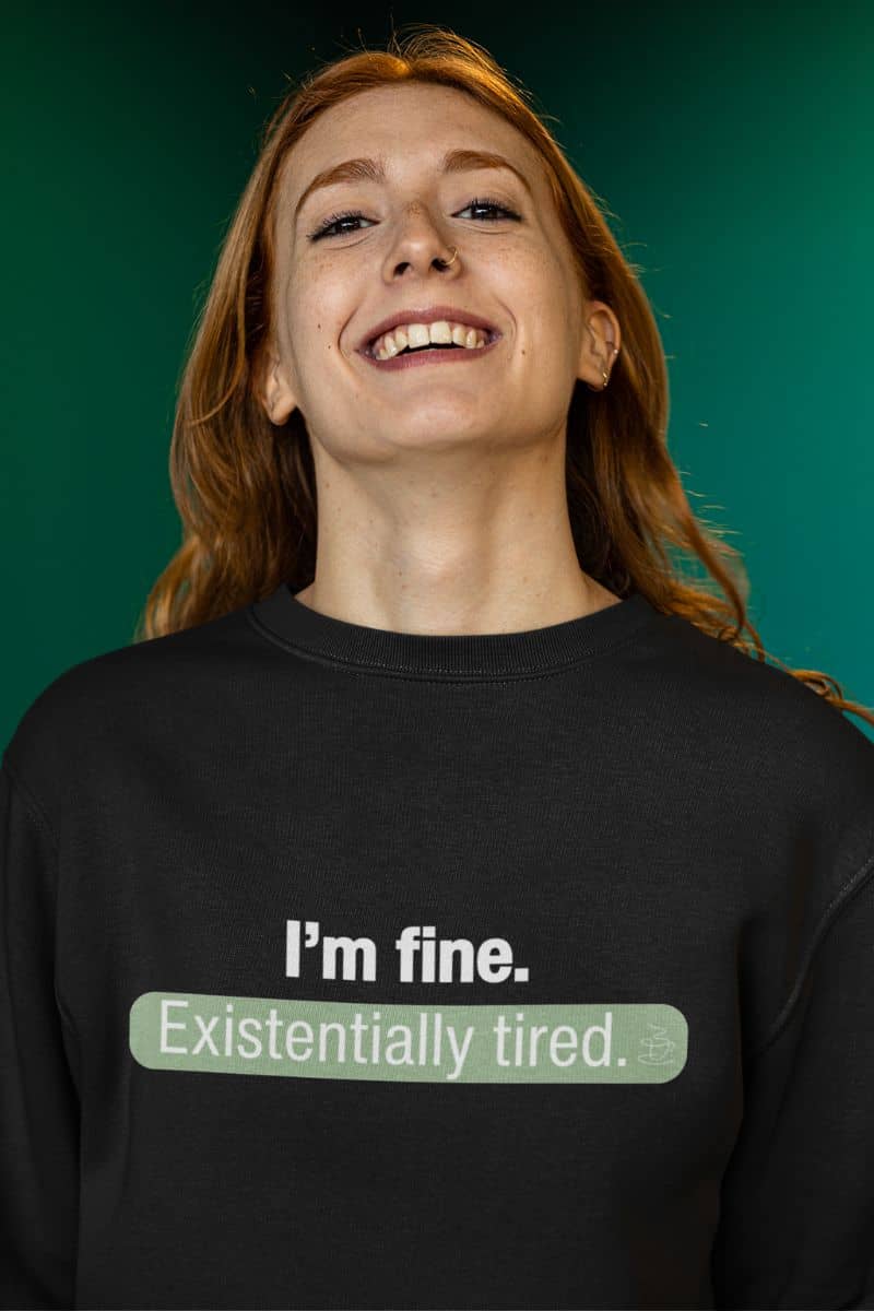 existential humor hoodie with a person wearing a black sweatshirt with humorous text 'I’m fine. Just existentially tired' on a teal background