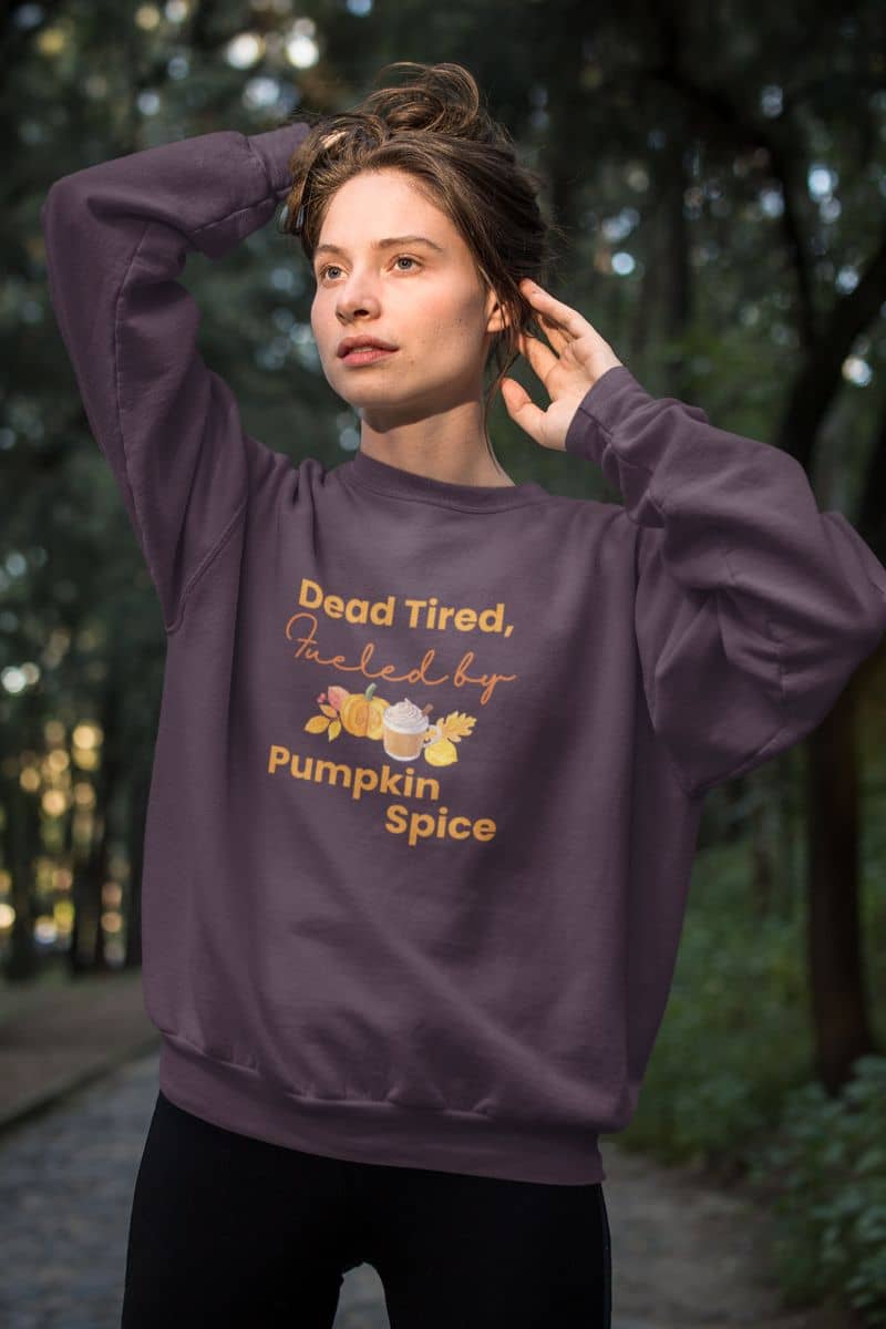 funny fall outfit with a person wearing a purple sweatshirt with 'Dead Tired, Fueled by Pumpkin Spice' text in a forest setting