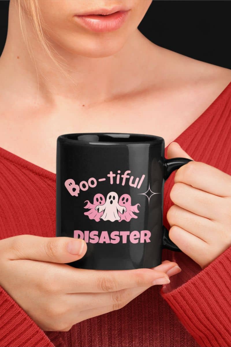 funny halloween coffee mug with a person holding a black mug with 'Boo-tiful Disaster' text and ghost design.