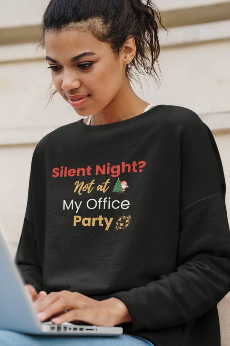 funny holiday pullover with a young girl in a black sweatshirt with humorous text 'Silent Night? Not at My Office Party', using a laptop.
