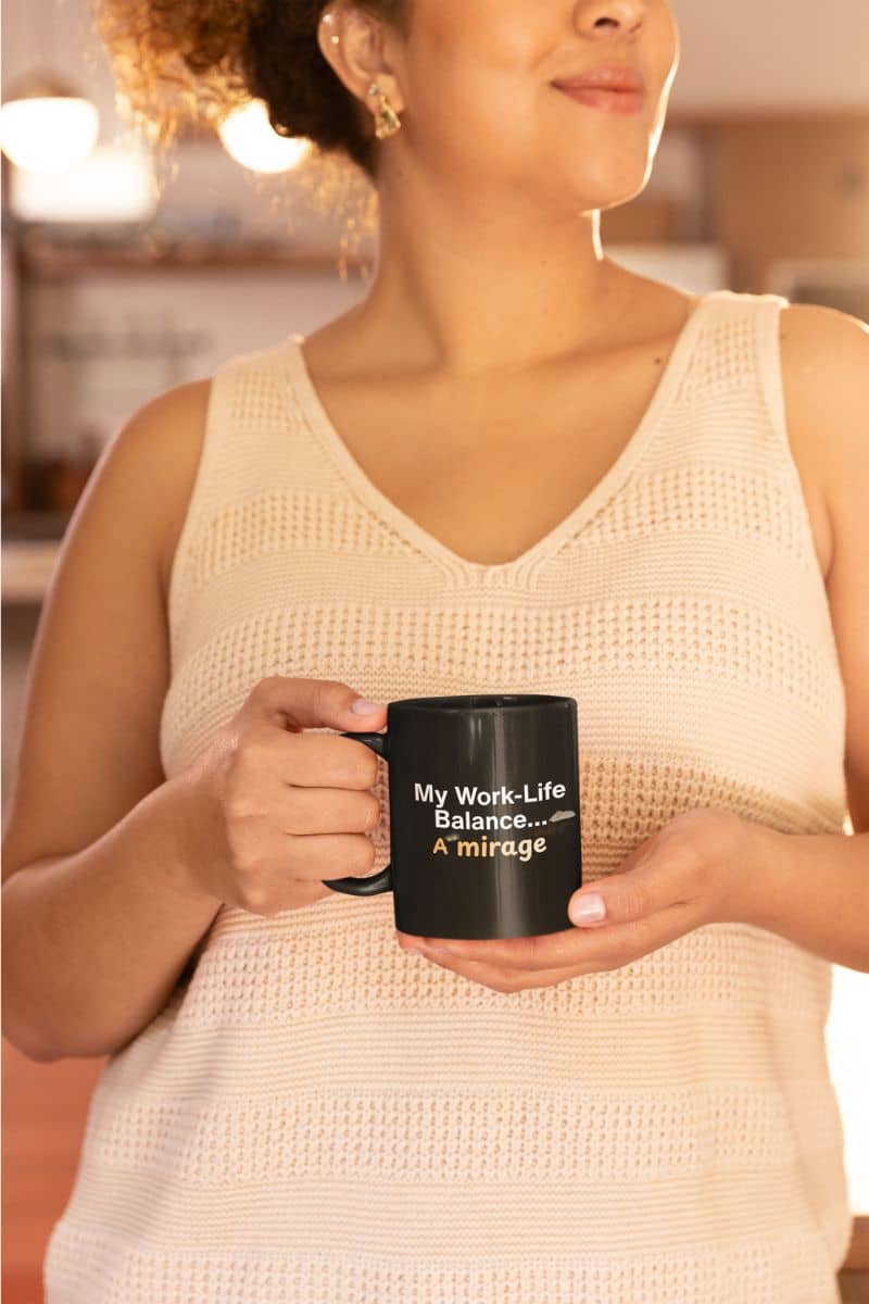 funny remote worker cup with a woman holding a black mug with text, wearing a beige sleeveless top.