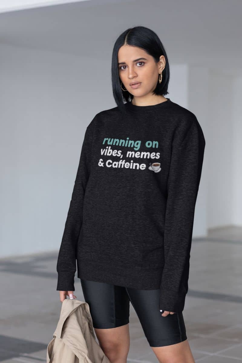 funny sweatshirt with a woman wearing a black sweatshirt with text 'Running on Vibes, Memes & Caffeine', standing against a plain background