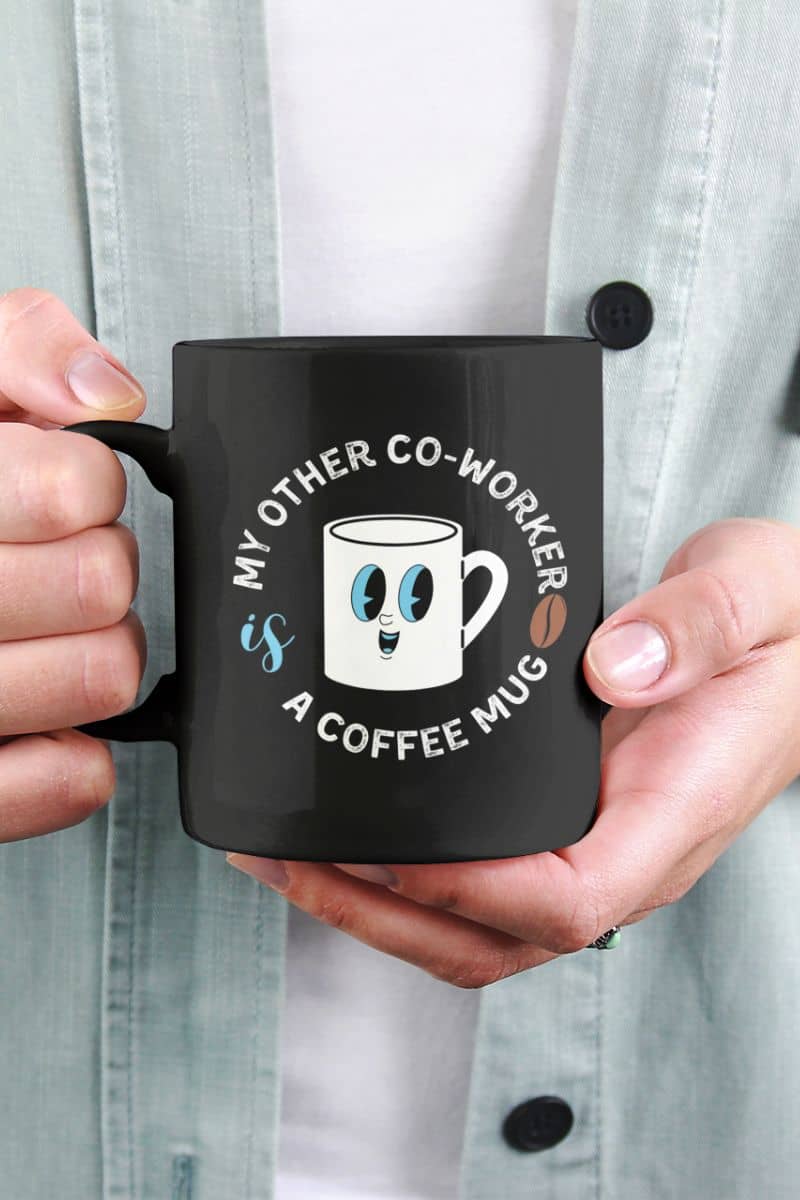 gag gift coffee mugs with a black mug with a humorous design held by hands against a light gray shirt background