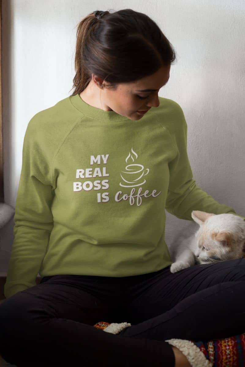 graphic coffee sweatshirt with a person wearing a green sweatshirt with a coffee-themed design, sitting with a cat.