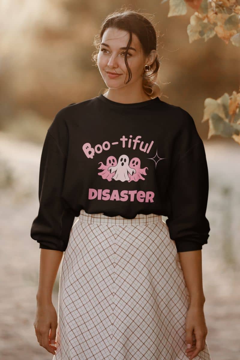 halloween ghost sweater with a woman wearing a black sweatshirt with 'Boo-tiful Disaster' text and ghost graphics outdoors.