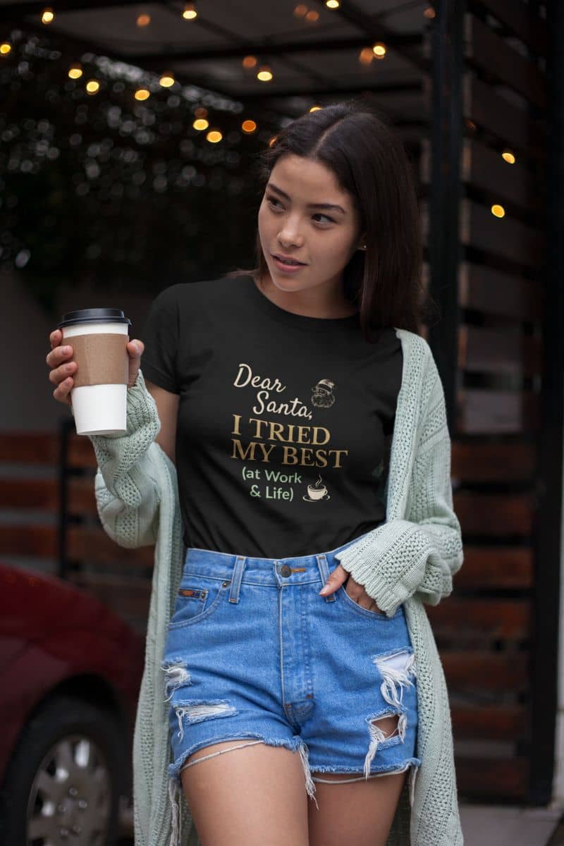holiday burnout shirt with a woman wearing a black t-shirt with text, holding a coffee cup, standing outdoors.