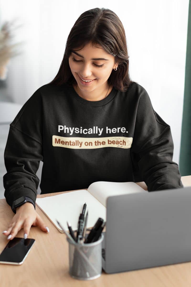 humor travel pullover with a person wearing a black sweatshirt with humorous text, sitting at a desk with a laptop and phone.
