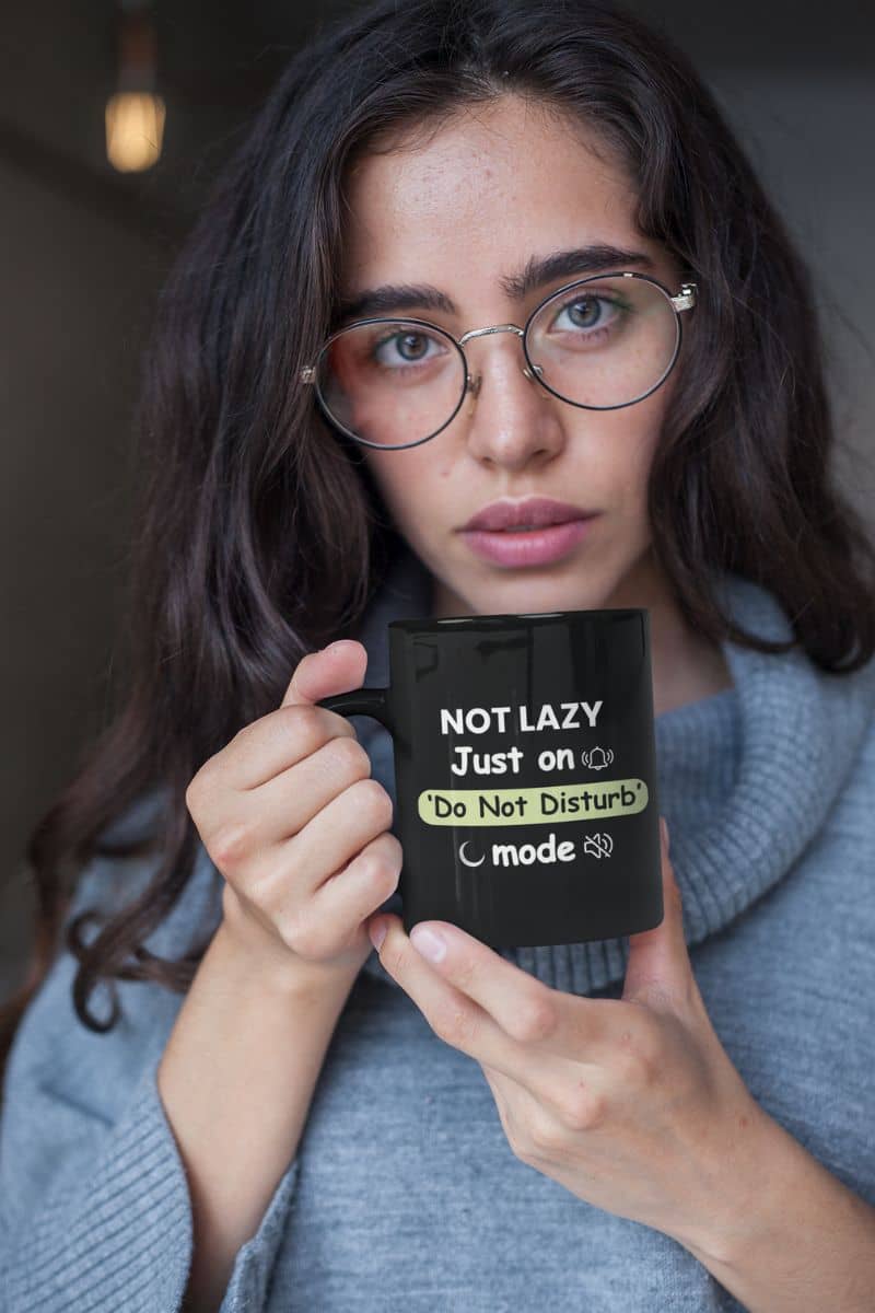 introvert coffee mug with a woman holding a mug with text 'Not Lazy, Just on Do Not Disturb mode' in a casual setting.