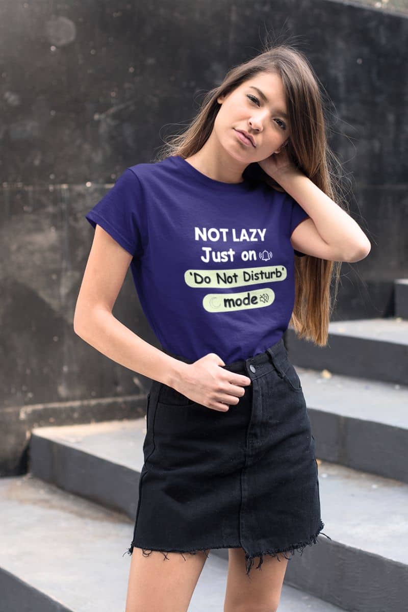 introvert quote shirt with a woman wearing a purple t-shirt with text 'NOT LAZY, Just on 'Do Not Disturb' mode', standing against a black wall.