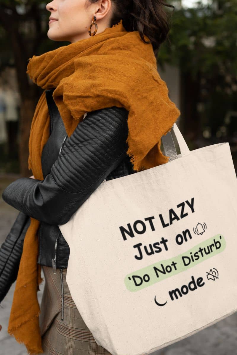 leave me alone tote with a person wearing a mustard yellow scarf and holding a tote bag with humorous text 'NOT LAZY, Just on 'Do Not Disturb' mode'.