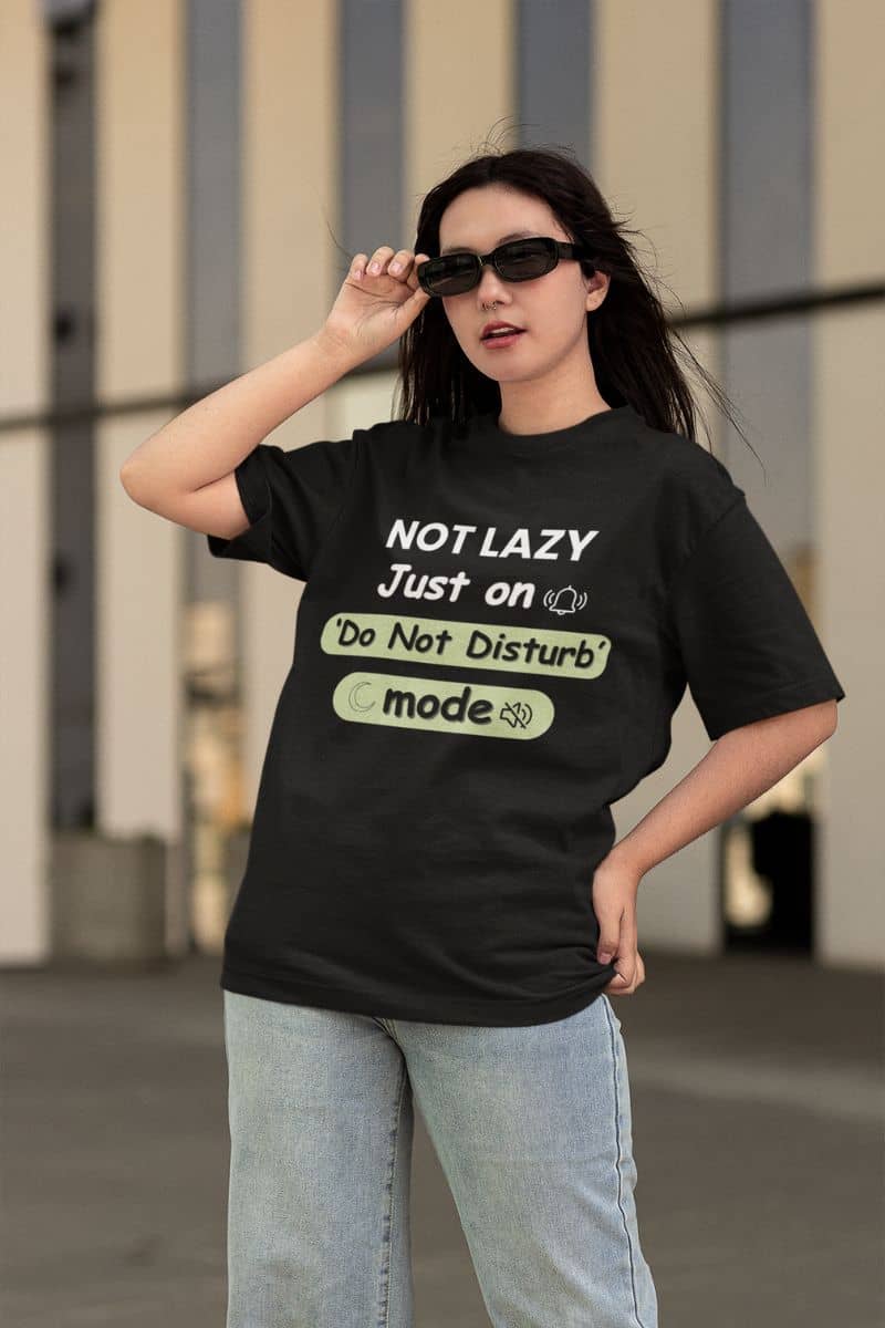 low energy lifestyle shirt with a person wearing a black t-shirt with humorous text 'NOT LAZY, Just on 'Do Not Disturb' mode' design outdoors.