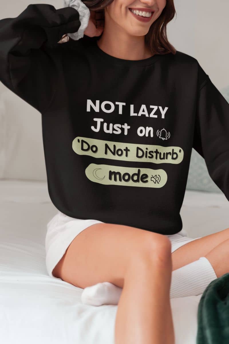 mental health crewneck with a person wearing a black sweatshirt with text 'NOT LAZY, Just on 'Do Not Disturb' mode' sitting on a bed.