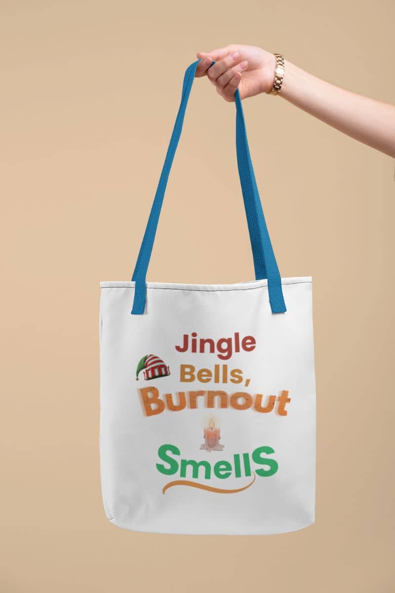 mental health tote with a tote bag with humorous text 'Jingle Bells, Burnout Smells' held by a hand against a beige background