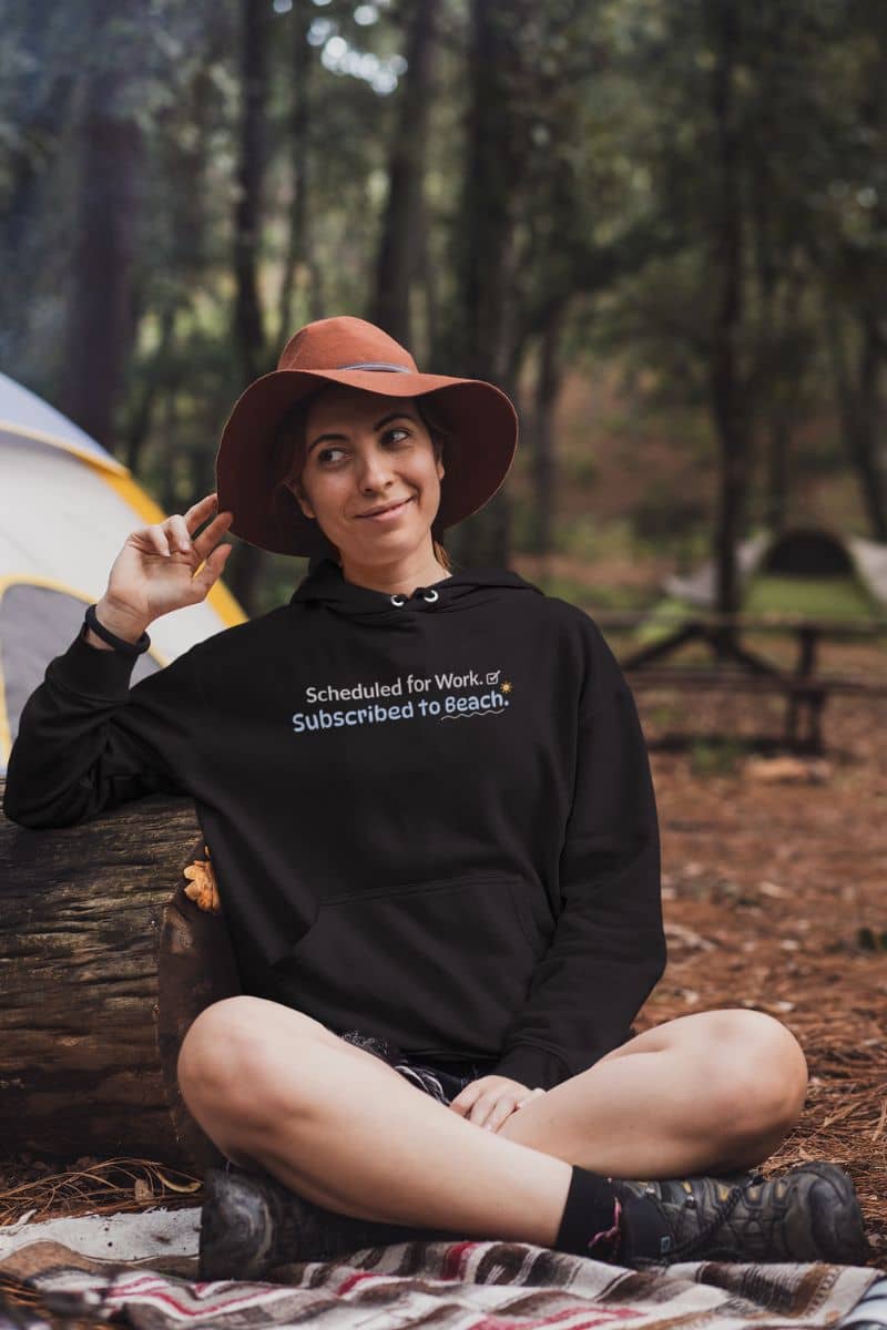 office humor vacation hoodie with a person sitting in a forest wearing a black hoodie with text and a wide-brimmed hat.