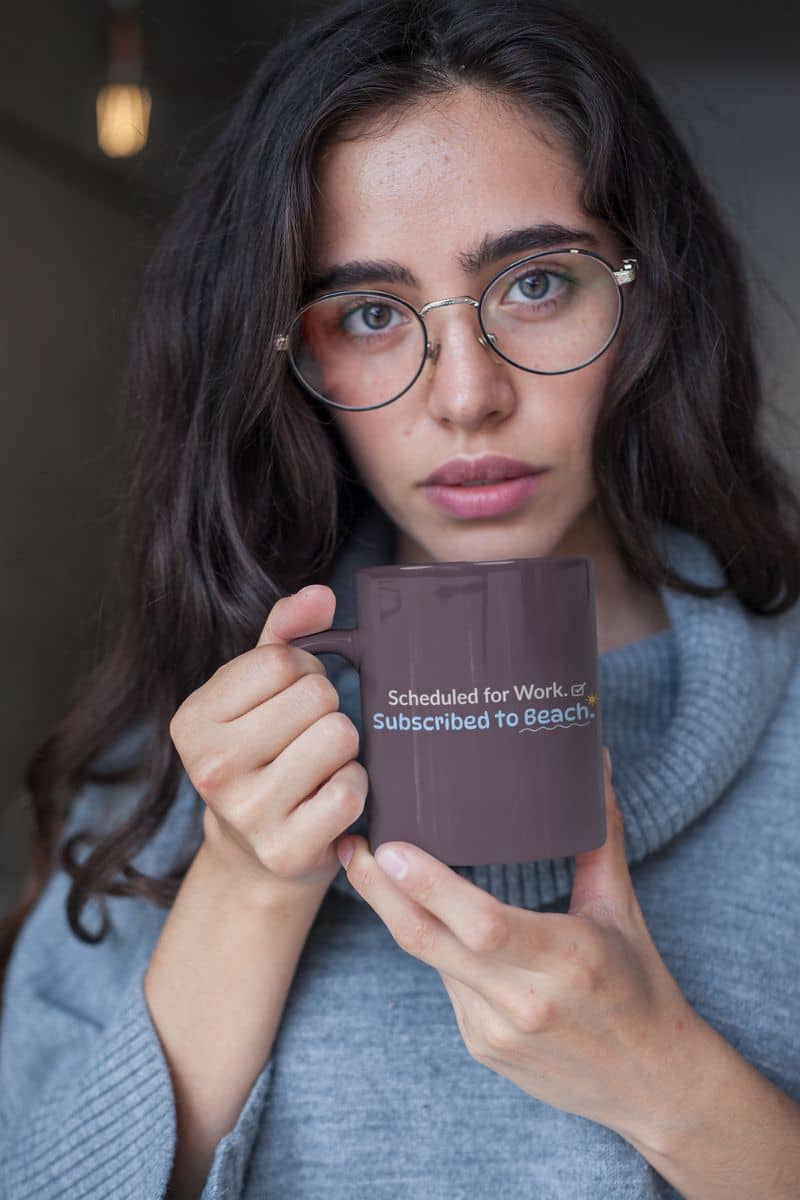 personalized travel mugs with a woman holding a mug, displaying the text 'Scheduled for Work. Subscribed to Beach', wearing glasses and a gray sweater.