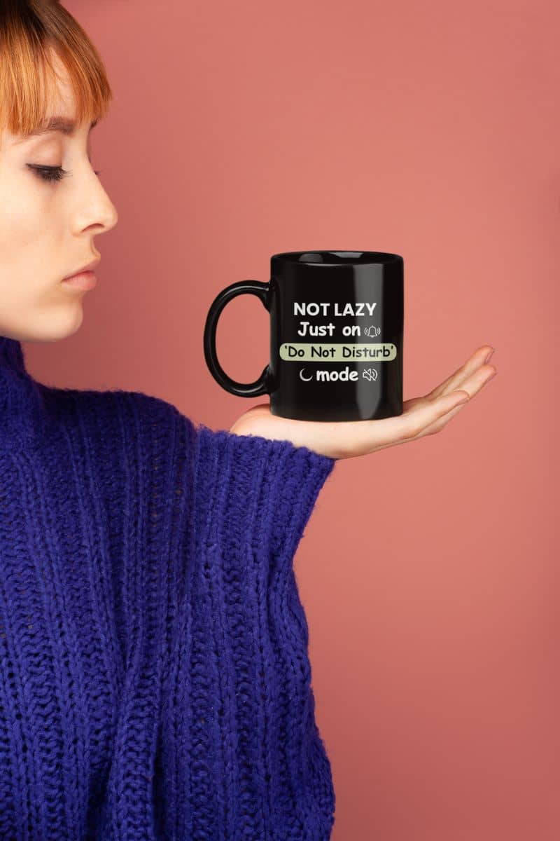 quiet morning mug with a person holding a black mug with text 'Not Lazy, Just on 'Do Not Disturb' mode' against a pink background