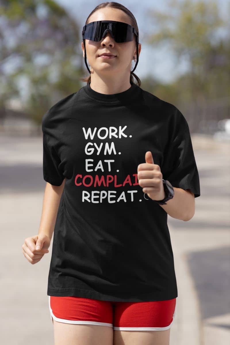 relatable quote shirt with a person wearing a black t-shirt with text 'Work. Gym. Eat. Complain. Repeat', giving a thumbs up outdoors.