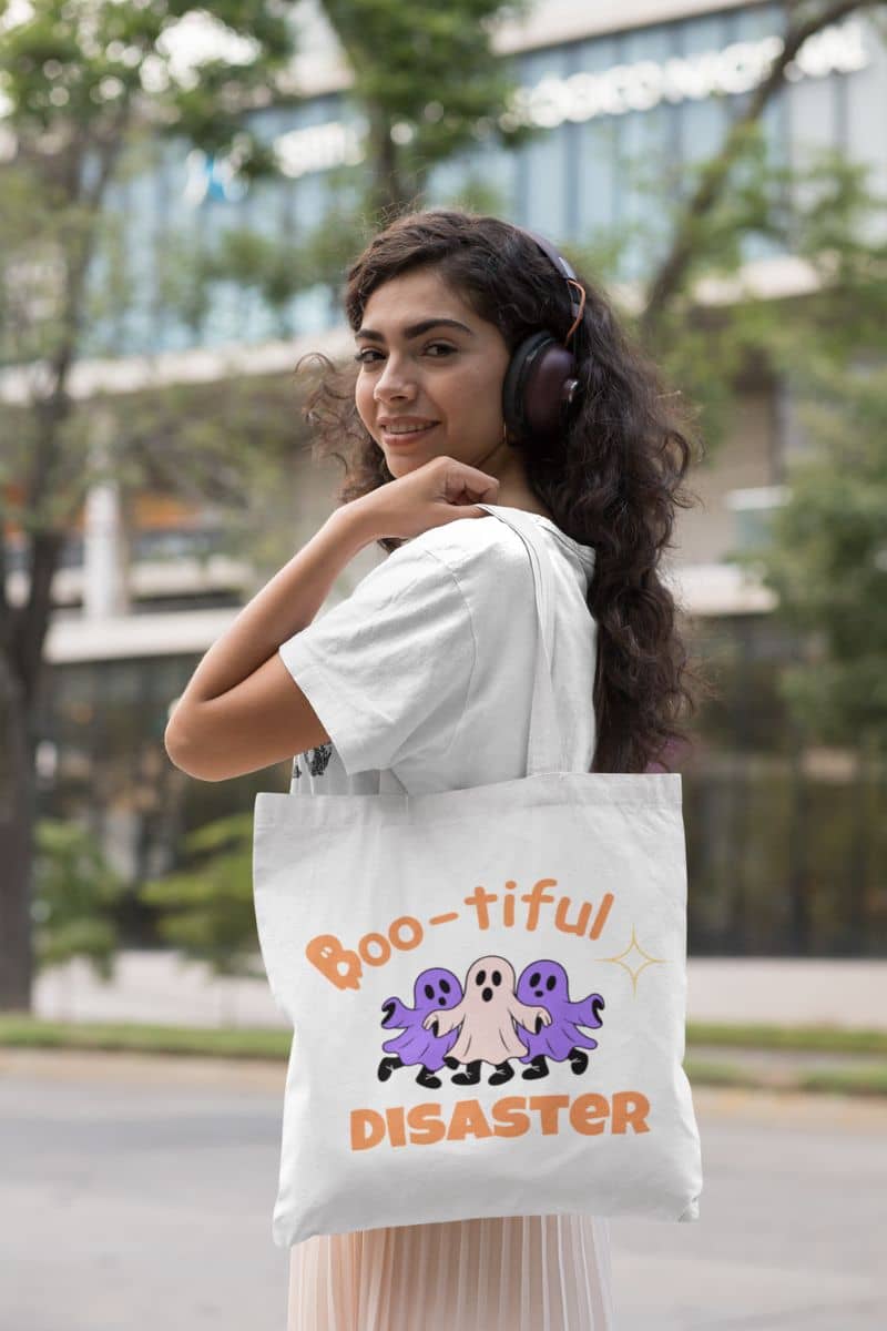 reusable halloween tote with a woman holding a tote bag with 'Boo-tiful Disaster' design outdoors.
